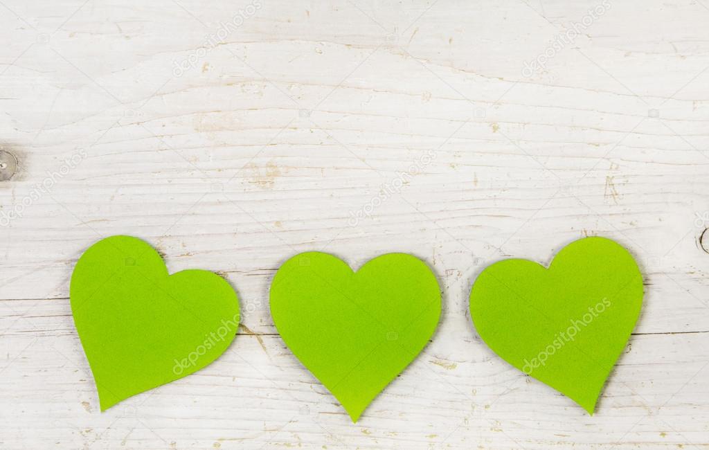 Three apple green hearts on white shabby style wooden background