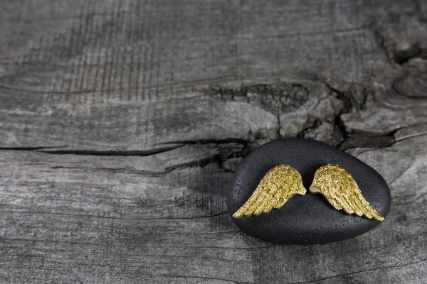 Ali d'angelo dorate su una pietra nera con sfondo grigio in legno . — Foto Stock