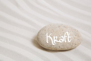 Stone in the sand with the german word power. Idea background fo clipart