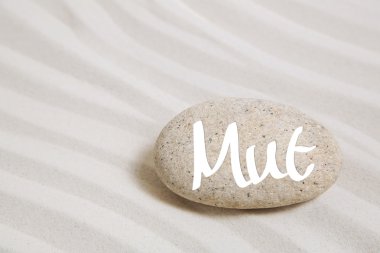 Sand background with a stone and the german word for courage.  clipart