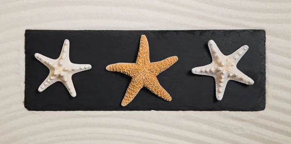 Summer beach concept: three starfishes on a black board for deco — Stock Photo, Image