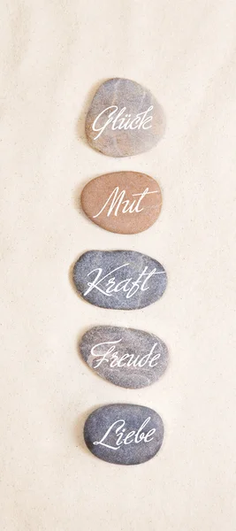 Five stones in the sand with the german words for luck, courage, — Stock Photo, Image