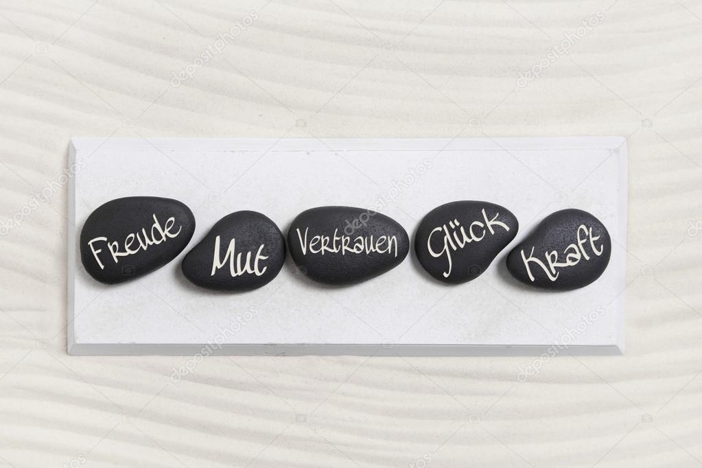 ive black stones with german text for happiness, courage, trust,