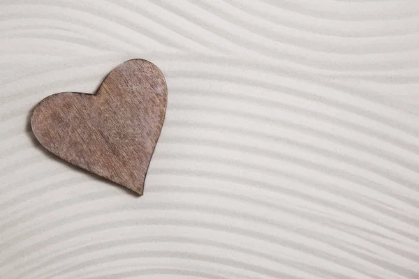 Een houten hart in het zand voor een achtergrond. — Stockfoto