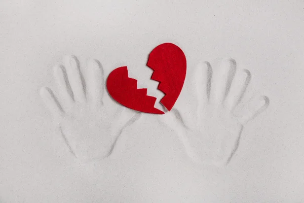 Broken red heart with hand prints in the sand for love sickness — Stock Photo, Image