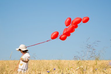 Child with flying red heart balloons on the blue sky background.