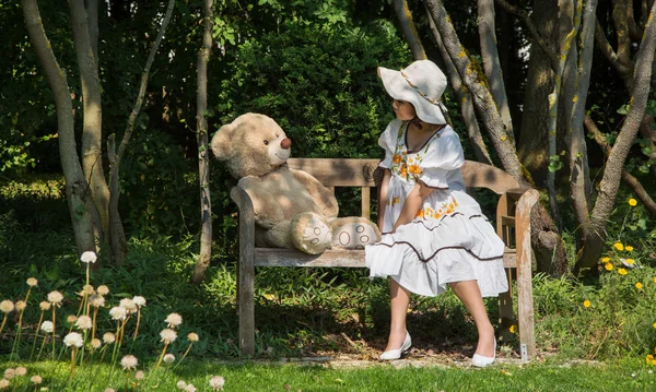 Little cute girl with her teddy bear sitting on a wooden bench i — 图库照片