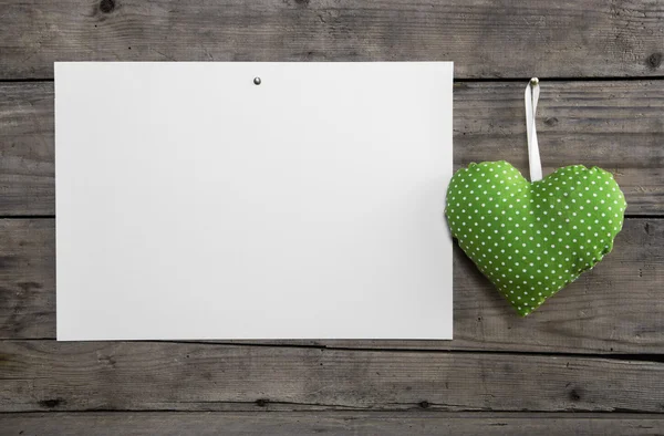 White paper on an old wooden wall with a lime green hanging hear 스톡 이미지