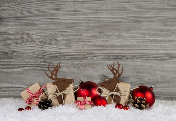 Piros karácsonyi dekoráció, vidéki stílusú díszdobozok, a jávorszarvas és a golyó a havas szürke fából készült háttér. — Stock Fotó