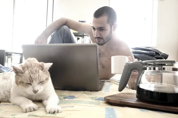Hombre usando el ordenador portátil en su cama mientras bebe café —  Fotos de Stock