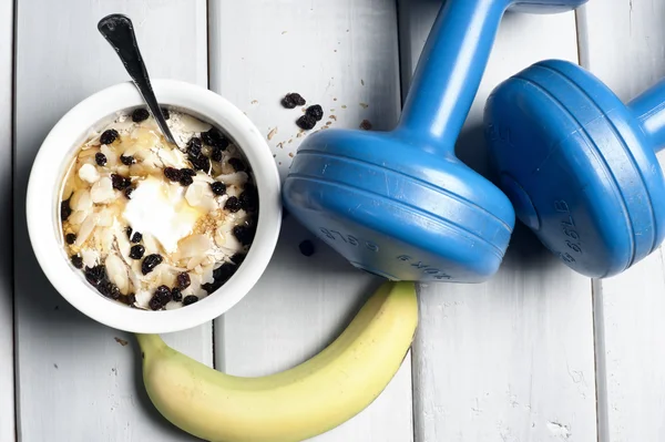 Dumbbells and banana next to bowl with yogurt — Stock Photo, Image