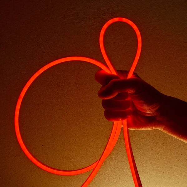 Flexible red led tape neon in hand on black background.