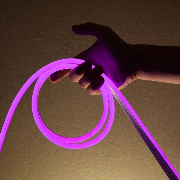 Flexible purple led tape neon in hand on black background.