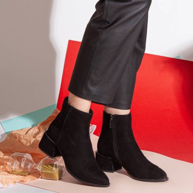 Siyah pantolonlu kadın bacakları ve orta topuklu siyah kısa ayakkabılar stüdyoda renkli bir arka plana karşı duruyor..