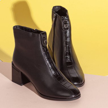 Bej arka planda, orta topuklu, kısa çizmeli bir çift siyah kadın..