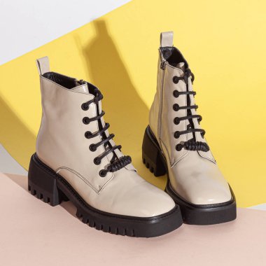 Bej arka plan stüdyo çekimlerinde orta topuklu yeni beyaz kadın kısa botları..