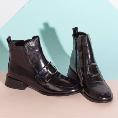 Bej arka planda, orta topuklu, kısa çizmeli bir çift siyah kadın..