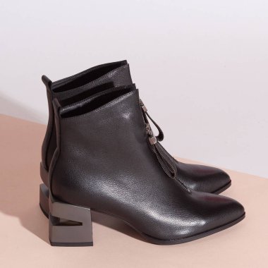 Bej arka planda, orta topuklu, kısa çizmeli bir çift siyah kadın..