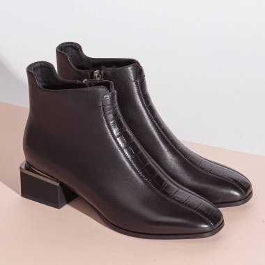 Bej arka planda, orta topuklu, kısa çizmeli bir çift siyah kadın..