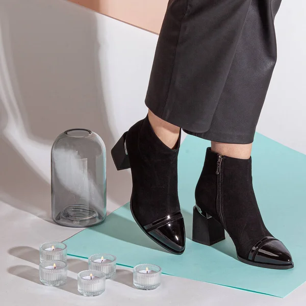 Women's legs in black pants and black short shoes on medium heel stands in the studio against a colored background.