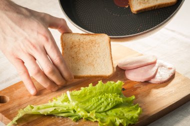 Ekmek, peynir, salata, jambon ve ahşap kesme tahtasıyla sandviç yapmak..