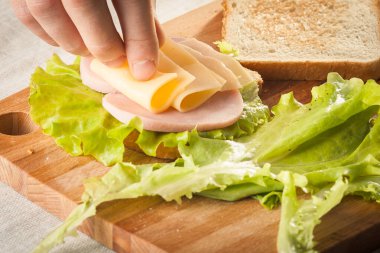 Ekmek, peynir, salata, jambon ve ahşap kesme tahtasıyla sandviç yapmak..