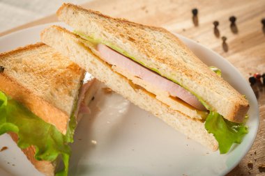 Cut by half sandwich with cheese, salad and ham.