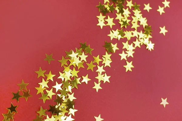 Close up golden star confetti on red background. Greeting card for Christmas, New Year and birthday. Copyspace.
