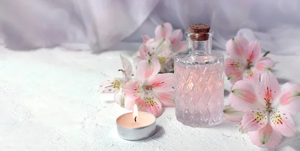 Mock up spa aromatherapy concept with perfume glass or aroma oil glass, flowers and candle on light background. Massage. Wellness. Spring greeting card for Mothers day or wedding.