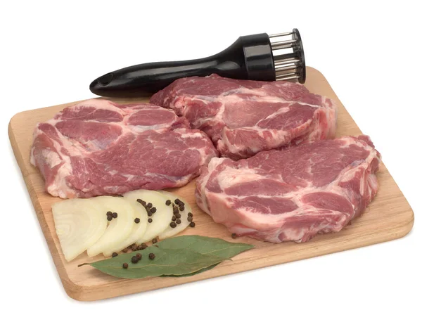 Tři kusy syrového vepřového masa s černým pepřem, cibulí a bobkovým listem na dřevěné desce — Stock fotografie