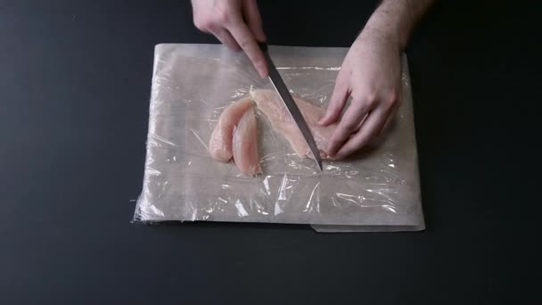 Человек режет грудку сырого цыпленка ножом — стоковое видео