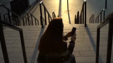 Bir telefon ile belgili tanımlık merdiven üzerinde oturan kız