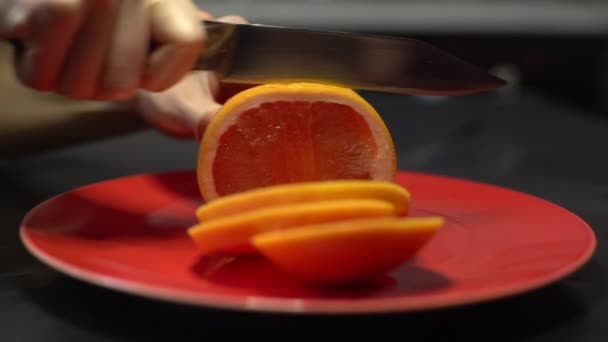 Messer schneiden Orange auf einem Teller auf einem roten runden Teller — Stockvideo