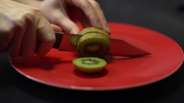 Cuchillo cortado kiwi fruta en un plato redondo rojo — Vídeos de Stock