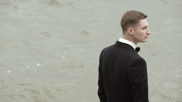 Visão traseira de um noivo em pé perto da água — Vídeo de Stock