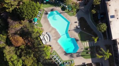 İnsansız hava aracı görüntüleri Los Angeles, Kaliforniya 'da lüks bir geometrik yüzme havuzunun üzerinde şezlonglar ve palmiye ağaçları ile yukarı doğru uçuyor. Sahne, çevresindeki modern yerleşim yerlerini ve bereketi gözler önüne seriyor.