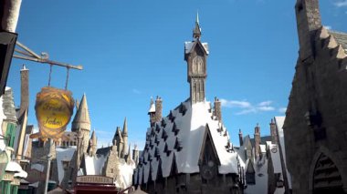 Karla kaplı çatıların manzarası ve parlak mavi gökyüzü altında fantezi şato tarzı mimari. Detaylı taş binalar ve dekoratif işaretler büyülü, masalsı bir atmosfer yaratıyor. Vuruldu.