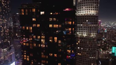 Geceleri Los Angeles şehir merkezindeki aydınlık gökdelenlerin, görünen logoları ve parlayan konut binaları olan yüksek katlı ofis kulelerinin hava aracı görüntüleri. Şehir ışıkları uzanıyor