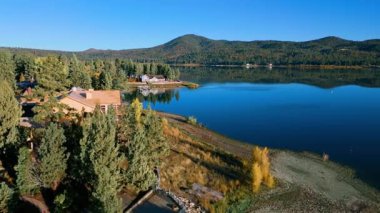 Hava aracı görüntüleri Güney Kaliforniya 'daki Big Bear Gölü' nün ormanlık kıyı şeridi boyunca sakin su ve ahşap rıhtımları gösteriyor. Kamera gölün üzerinde sorunsuzca hareket ediyor, yansımaları, evleri yakalıyor.