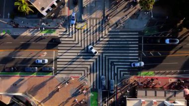Santa Monica, Los Angeles, Kaliforniya 'da yoğun bir yaya geçidinin insansız hava aracı görüntüsü. Yayalar şeritli yaya geçidinde yürürken arabalar kavşakta hareket ediyor.