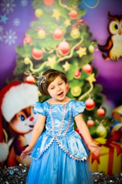 Karnaval prensesi elbisesi giymiş mavi gözlü, küçük, güzel bir kız, yeni yıl tatilinde manzaranın yanında duruyor.