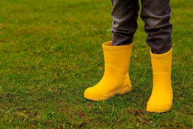 Sarı lastik çizmeli çocukların ayakları çimlerin üzerinde, yakın plan.