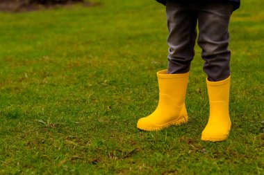 Sarı lastik çizmeli çocukların ayakları çimlerin üzerinde, yakın plan.