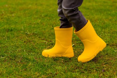 Sarı lastik çizmeli çocukların ayakları çimlerin üzerinde, yakın plan.