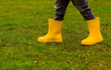 Sarı lastik çizmeli çocukların ayakları çimlerin üzerinde, yakın plan.