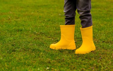 Sarı lastik çizmeli çocukların ayakları çimlerin üzerinde, yakın plan.
