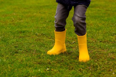 Sarı lastik çizmeli çocukların ayakları çimlerin üzerinde, yakın plan.