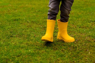 Sarı lastik çizmeli çocukların ayakları çimlerin üzerinde, yakın plan.