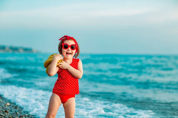 Маленька Дівчинка Червоному Купальнику Сонцезахисних Окулярах Стоїть Босоніж Пляжі Тримає Стокове Зображення