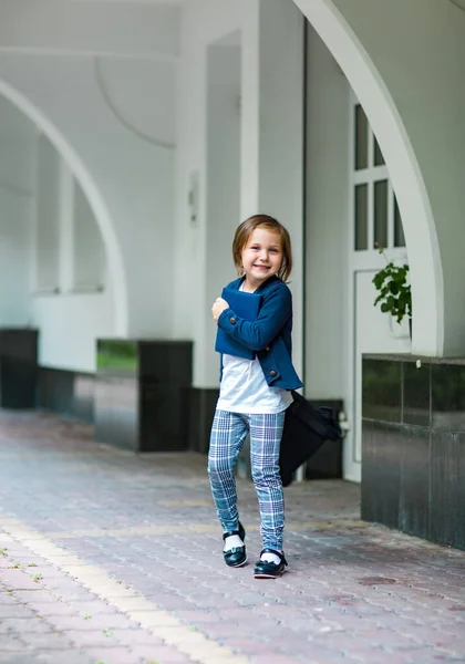 a beautiful little girl, a schoolgirl, in the afternoon near the school, in a stylish school uniform